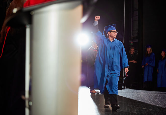Photo of TFS graduate walking across the stage in cap and gown
